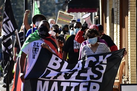 Protesters holding a black lives matter flag and walking