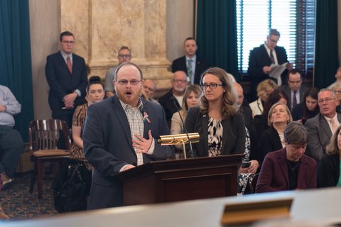 Man standing next to a woman at a podium speaking into microphone