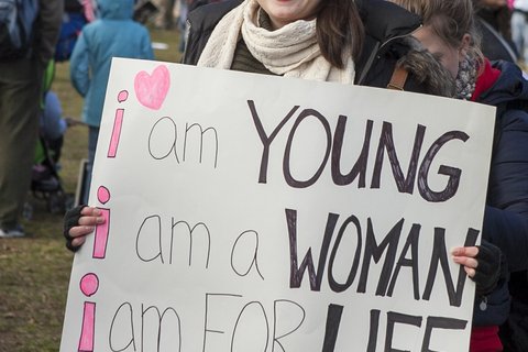 A white woman holding a sign saying "I am young, I am a woman, I am FOR life"