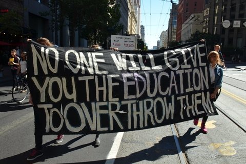 Protesters holding a banner that reads: No one will give you the education to overthrow them