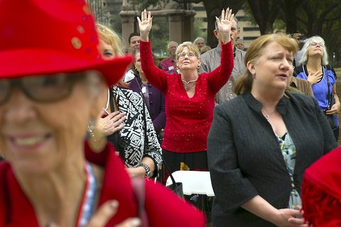 Older woman standing in crowd with both hands raised