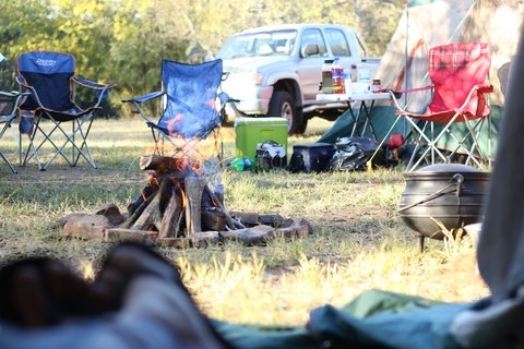 Stock photo of a camp with fire, camping chairs, the side of a tent, and a silver pickup truck in the background