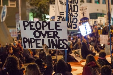 A protester holding a sign that reads "people over pipelines"