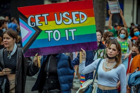 A woman at a Pride march in Paris holding a sign painting in the LGBT colors that says "Get used to it"