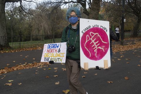 A person at a protest holding a sign that says DeGrow the North and Decolonize the south