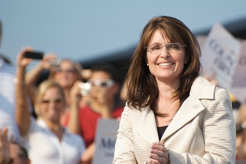 Sarah Palin in a white jacket, in front of a crowd, smiling.