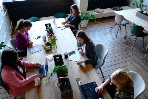 A group of women at a table, with computers and books.