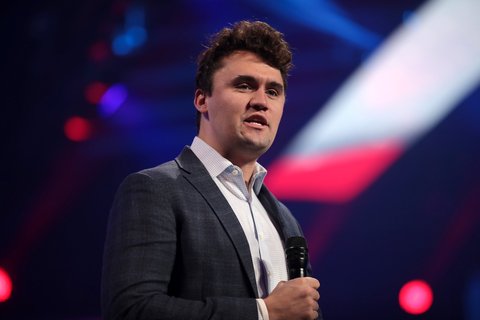 A young white man, Charlie kirk, in a suit, holding a mic.