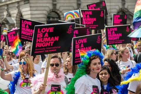 People in a protest wearing rainbow wigs, holding signs that say "love is a human right"