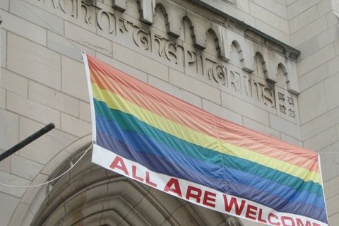 A rainbow flag outside a church with the words "All are welcome"