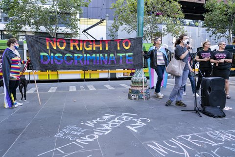 Protesters standing around a mic, two people holding a banner that reads "no right to discriminate"