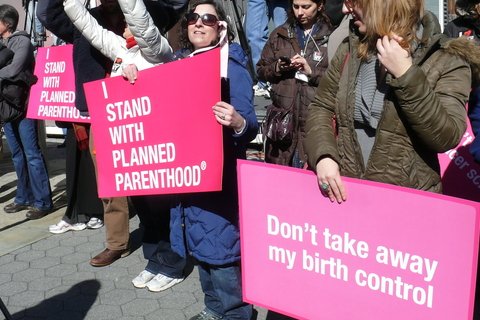 Protesters holding banners. One says I Stand with Planned Parenthood, another one says "Don't take away my birth control"