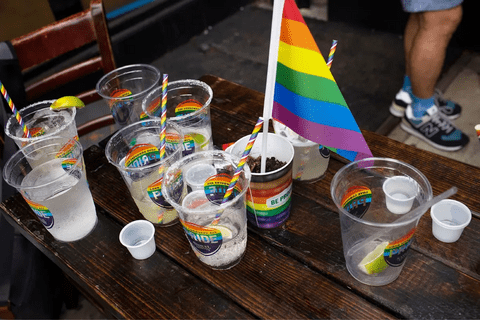 A table with plastic cups that have stickers on them that say "Pride." One of the cups has a rainbow flag in it.