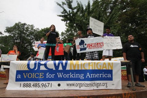 People standing on a platform with a table in front of them with a banner hanging off the table that says "A voice for Working America."