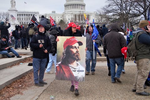 A woman wearing a Make America Great Again cap carrying an image of Jesus wearing a MAGA hat with "WWG1WGA" on his lapel