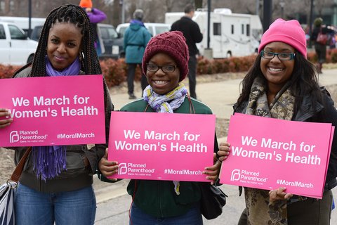 Three Black women wearing winter clothes holding signs that say "we march for Women's Health"