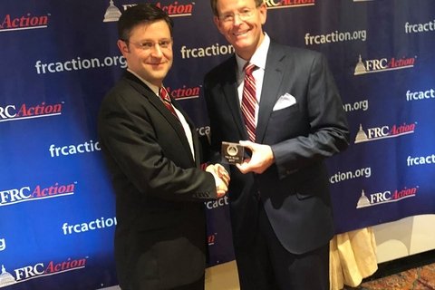 Two men in suits and glasses standing in front of a background saying "FRCAction"