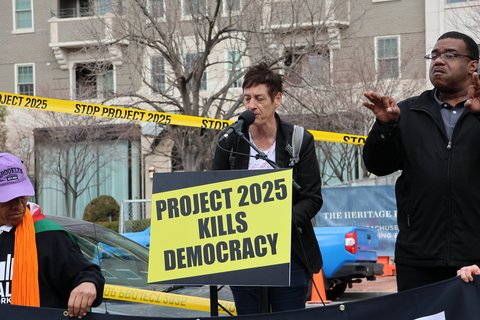 Two people on a podium with a board that reads "Project 2025 Kills Democracy"