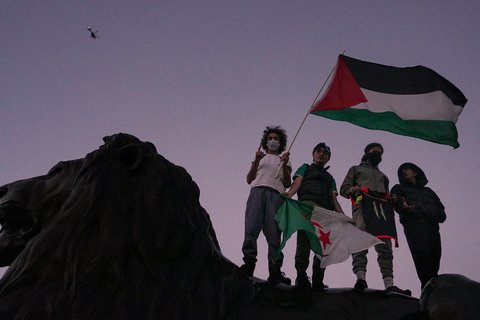 Four people carrying a Palestinian flag standing on a lion.