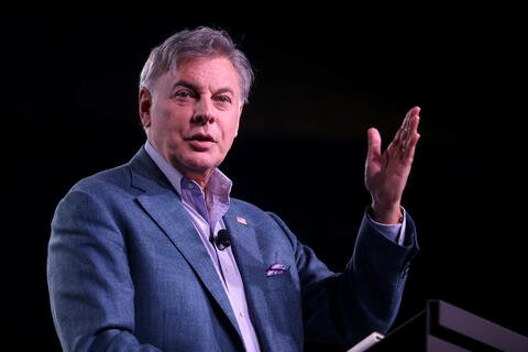 A man in a suit talking with his hand raised.