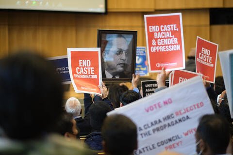 People holding banners that say "End Caste Discrimintaion" and "End Caste, Racial, And Gender Opression" and a picture of Dr. Ambedkar.
