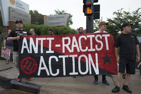 People holding a red and black flag that reads Anti-Racist Action