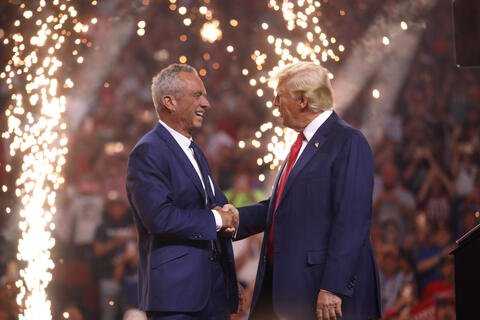Two men shaking hands with fireworks behind them.