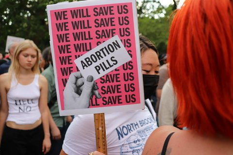 a sign that reads "We will save us" over and over again with a hand that holds a paper that says "Abortion Pills"