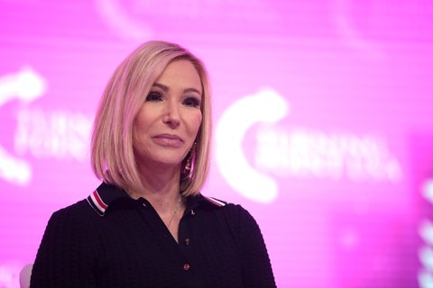 A woman in a black polo shirt with a pink background
