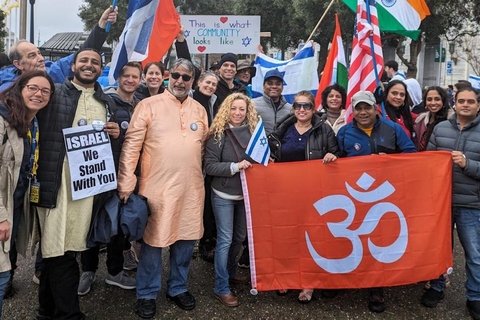 A group of people holding israeli flags and a big saffron flag with an om on it.
