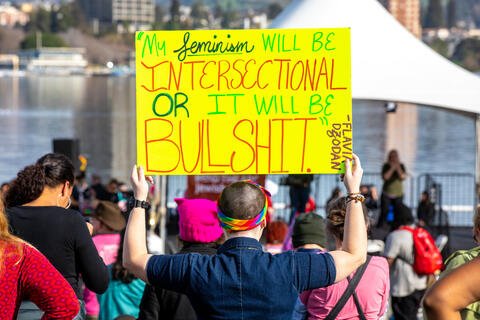 A person holding a yellow sign that reads "my feminism will be intersectional or it will be bullshit."