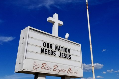 White sign against blue sky that reads "Our Nation Needs Jesus"