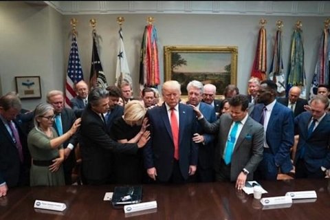President Trump surrounded by people touching him and bowing their heads