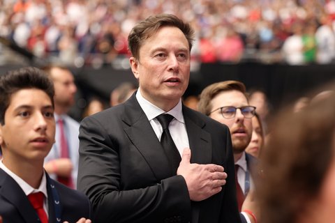 Elon Musk stands solemnly with hand on heart