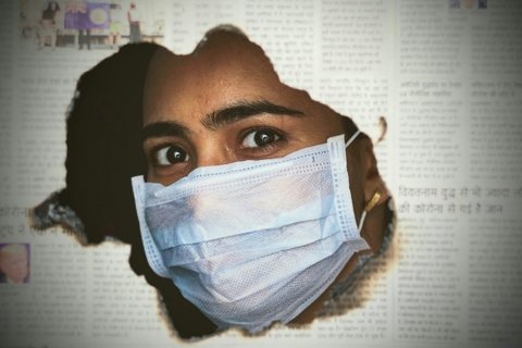 masked woman’s face peeks through hole in newspaper