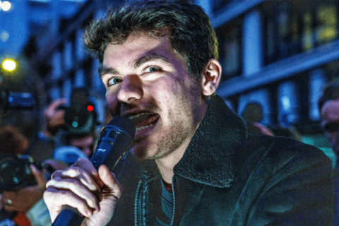 a man talking into a mic lit by a light in front of his face.
