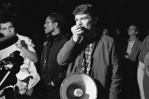 A black and white image of Nick Fuentes with a megaphone