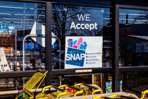 A window of a grocery store with a sign that reads "we accept SNAP"